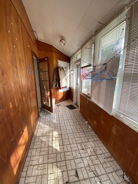 Sunroom with wood paneling, tile floor, windows with blinds, and a door.