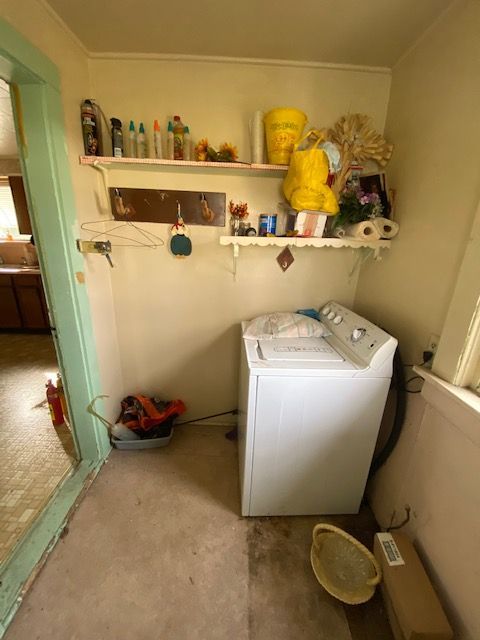 Laundry room with a washing machine, shelves with supplies, and a doorway.
