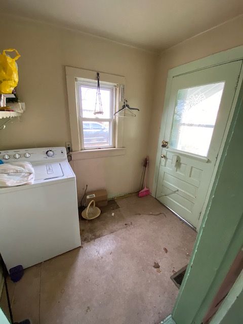 Laundry room with a washing machine, window, and door.  A broom and dirty floor are visible.