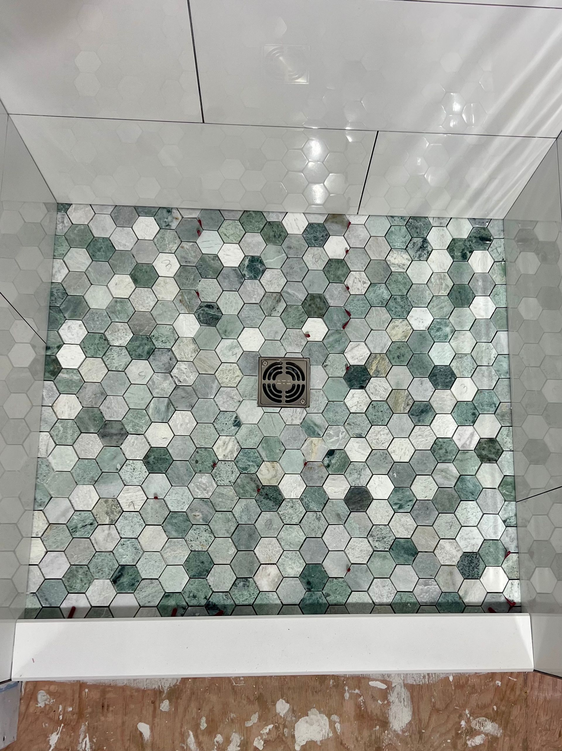 Shower base with green hexagon tiles, surrounded by white tile walls and a white curb.
