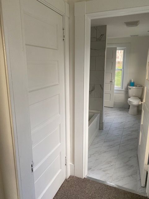 White door opening to a bathroom with tiled floor, white fixtures, and a window.