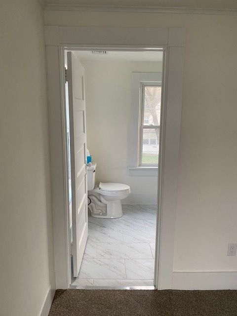 White doorway leading to a bathroom with a toilet, window, and white and gray flooring.