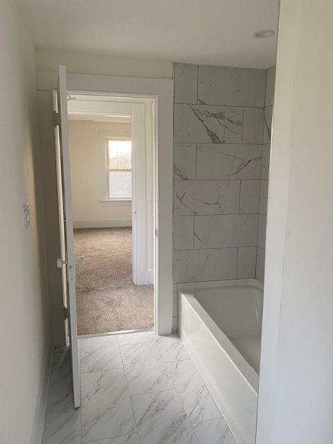 Bathroom with marble tile floor, bathtub, and doorway to carpeted room.