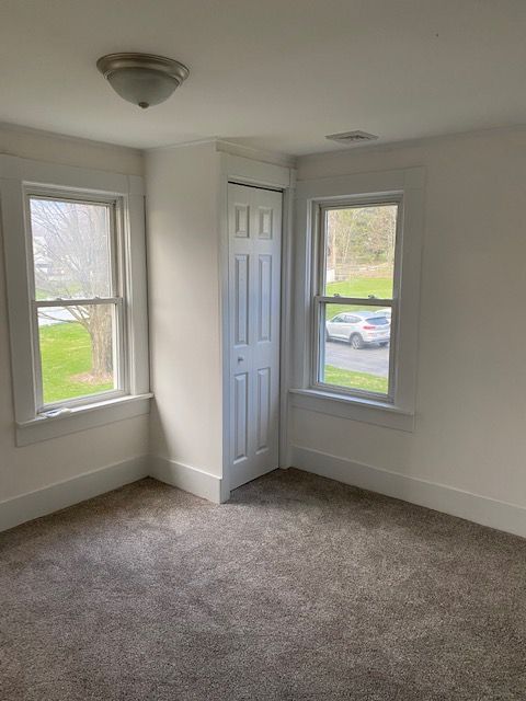 Empty bedroom with two windows, a closet door, white walls, and gray carpet.