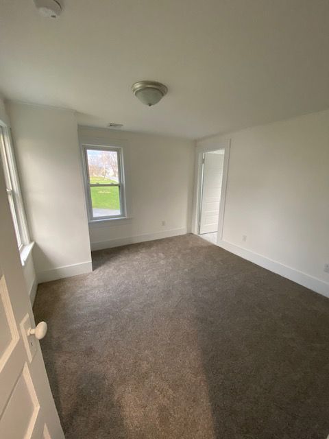 Empty room with brown carpet, white walls, a window, and a doorway.