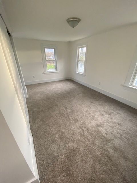 Empty bedroom with neutral carpet, white walls, and two windows.