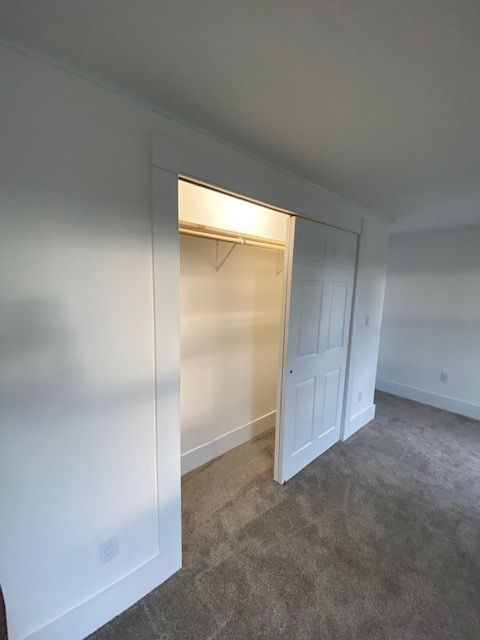 White sliding closet doors, open to reveal interior with a shelf and clothes rod. Beige carpet.
