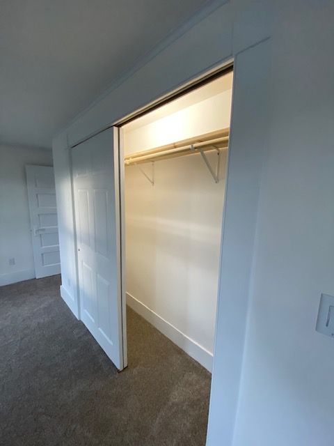 Closet with sliding doors, white trim and shelves, a clothing rod and carpeted floor.