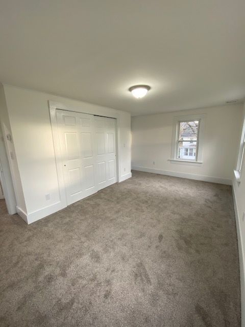 Empty bedroom with white walls, closet doors, and a window. Light brown carpet.