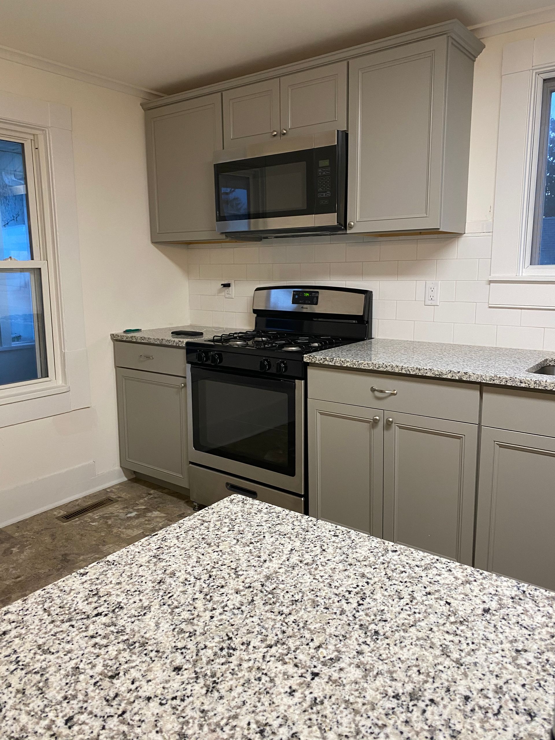 Gray kitchen cabinets with a granite countertop, stainless steel appliances, and white tile backsplash.