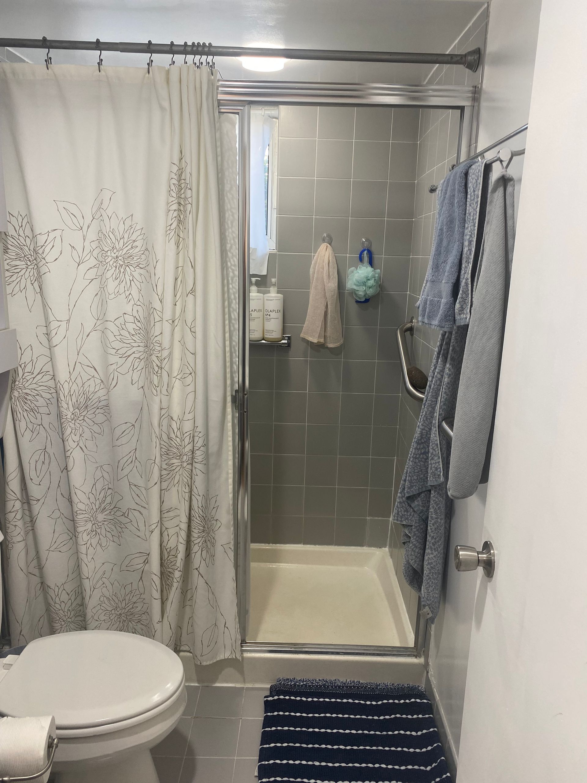 Small bathroom with a shower, toilet, and towels. Gray tile and a white shower curtain.