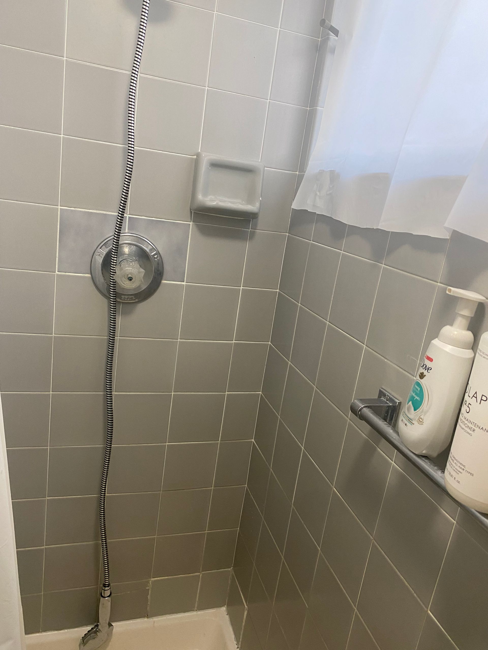 Gray-tiled shower with a showerhead, soap dish, and bottles on a shelf.