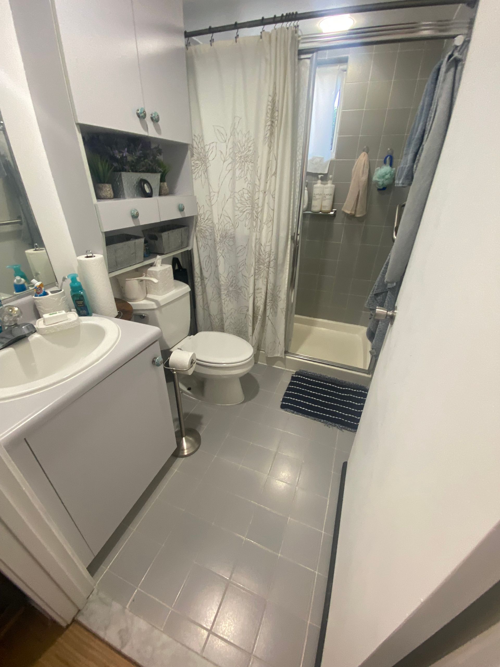 Bathroom with white cabinets, gray floor, toilet, sink, and shower with curtain.
