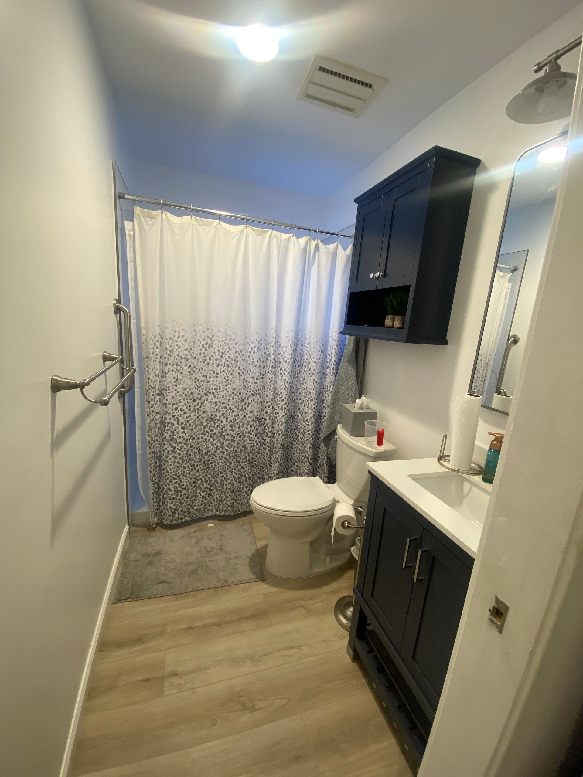 Bathroom with blue vanity, navy storage cabinet, white toilet, and patterned shower curtain.