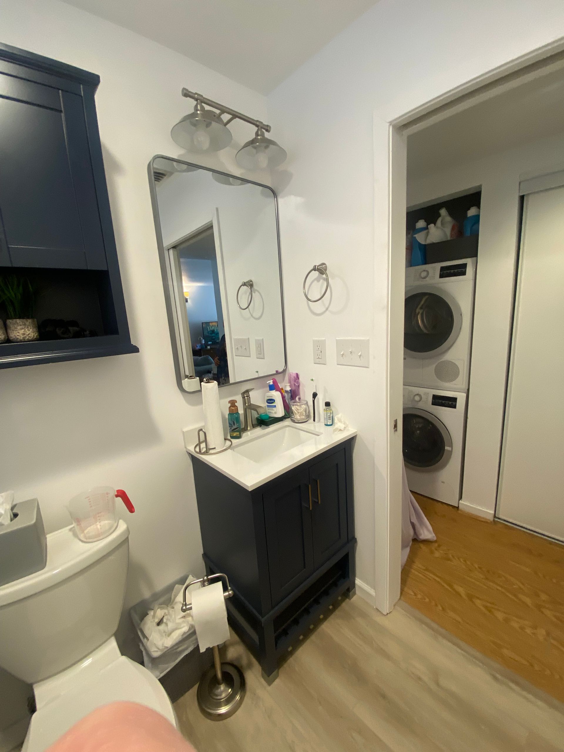 Bathroom with blue vanity, mirror, and stacked washer/dryer visible in doorway.