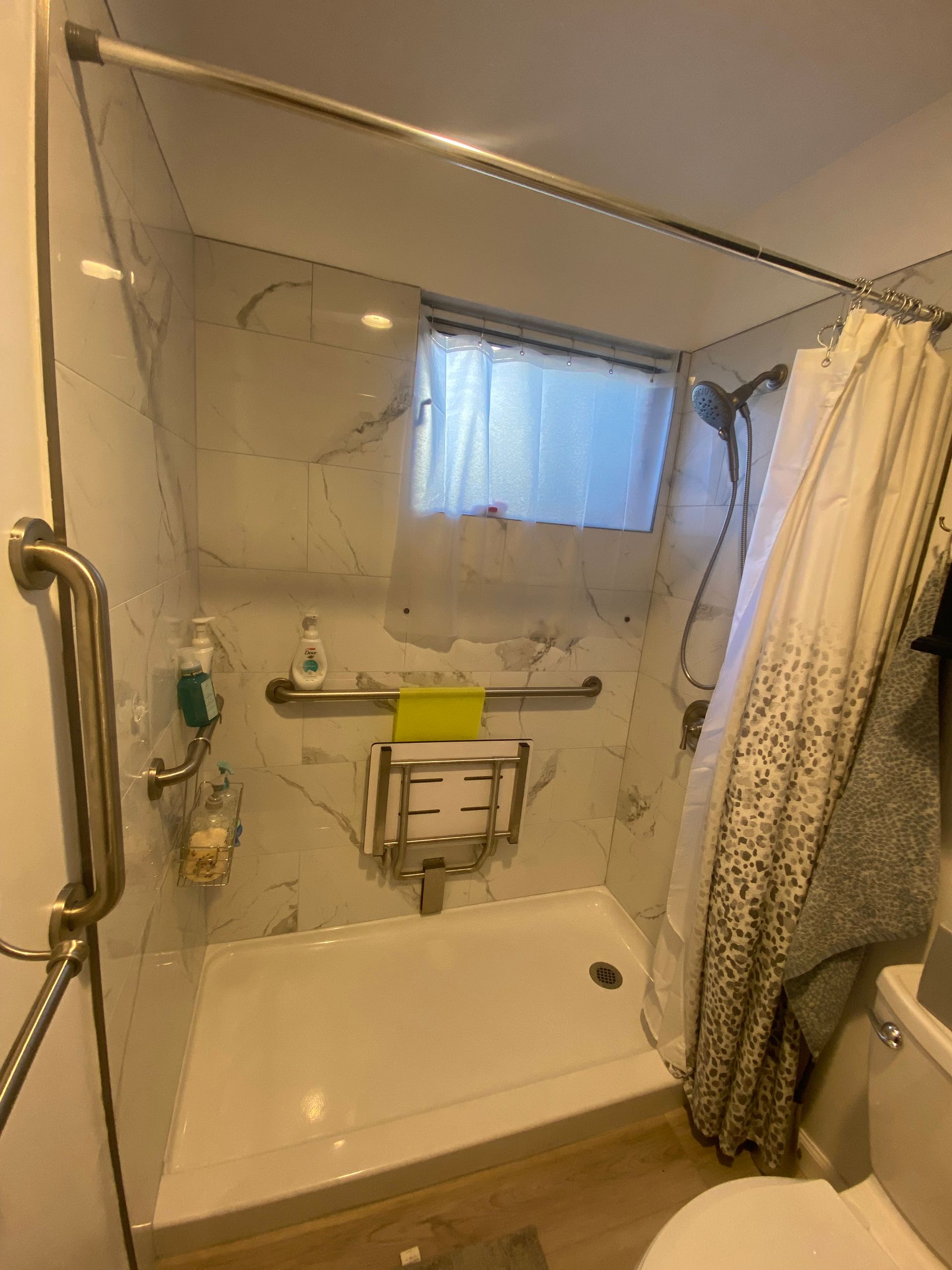 Accessible shower with grab bars, fold-down seat, and shower curtain. Marble-like tile.