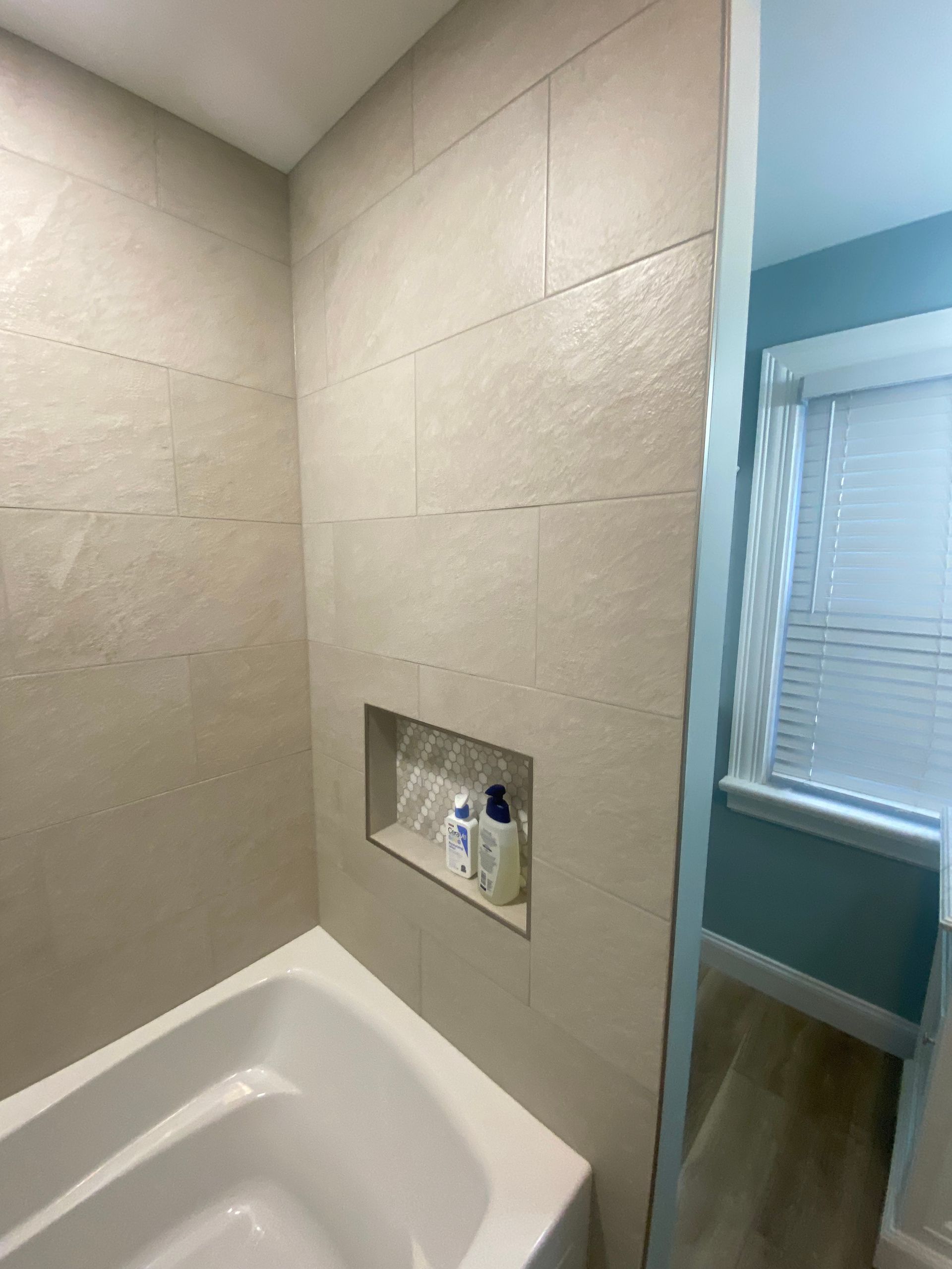 Bathroom with light beige tiled walls, a recessed shelf, and a white bathtub.
