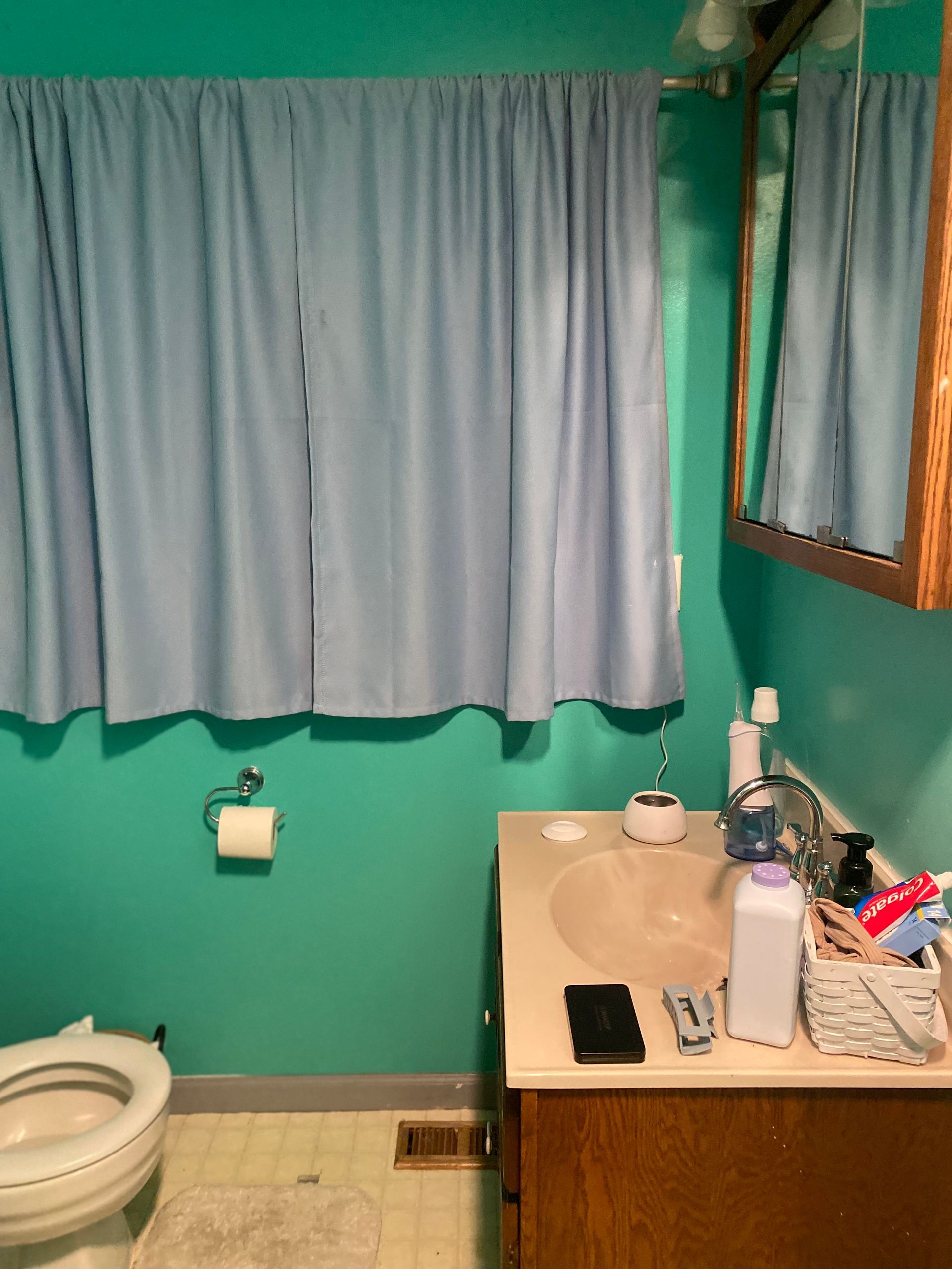 Small bathroom with teal walls, light blue curtains, and a wooden vanity.