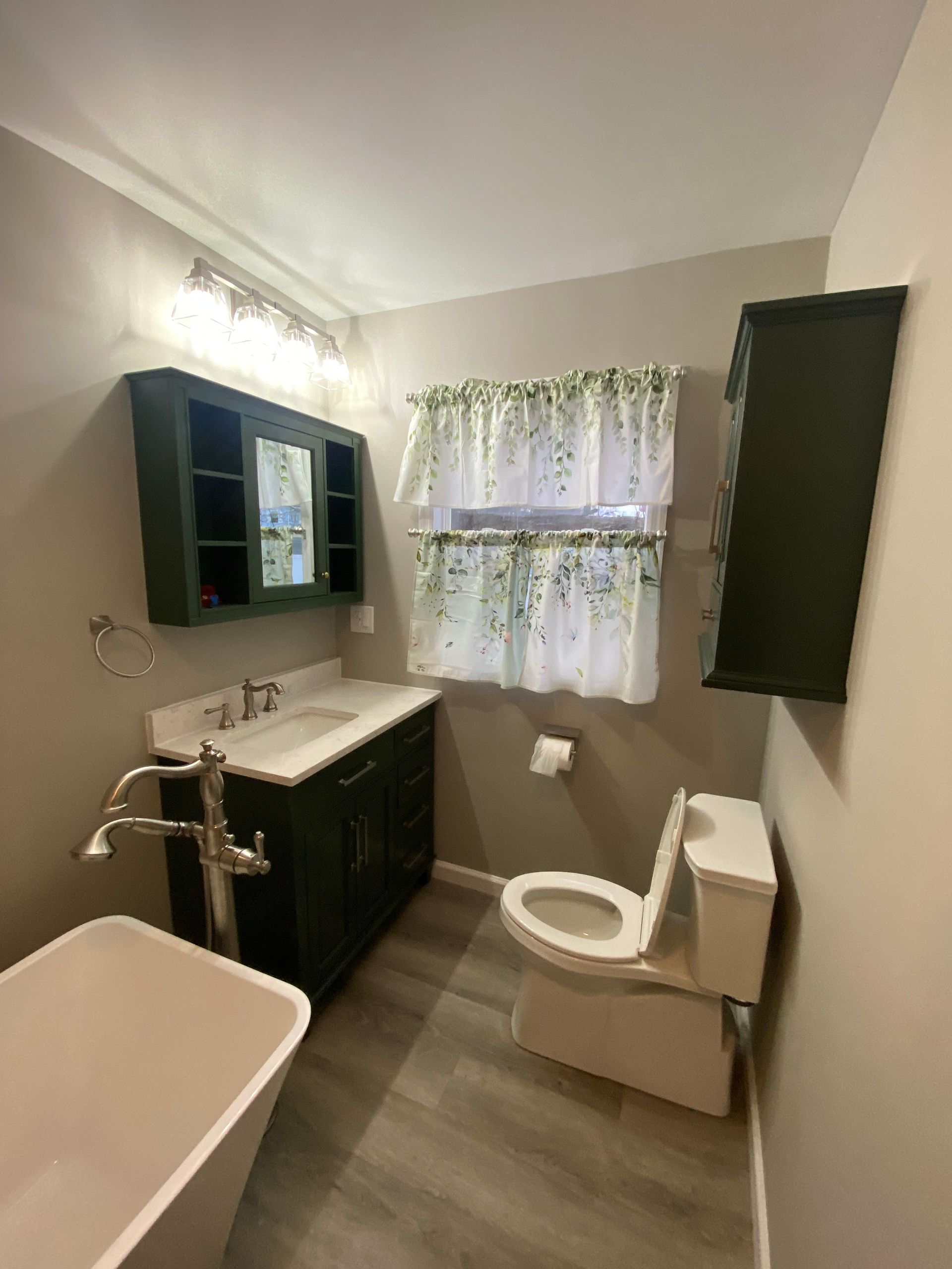Bathroom with a dark green vanity, cabinet, and wall storage. Features a white toilet and tub.