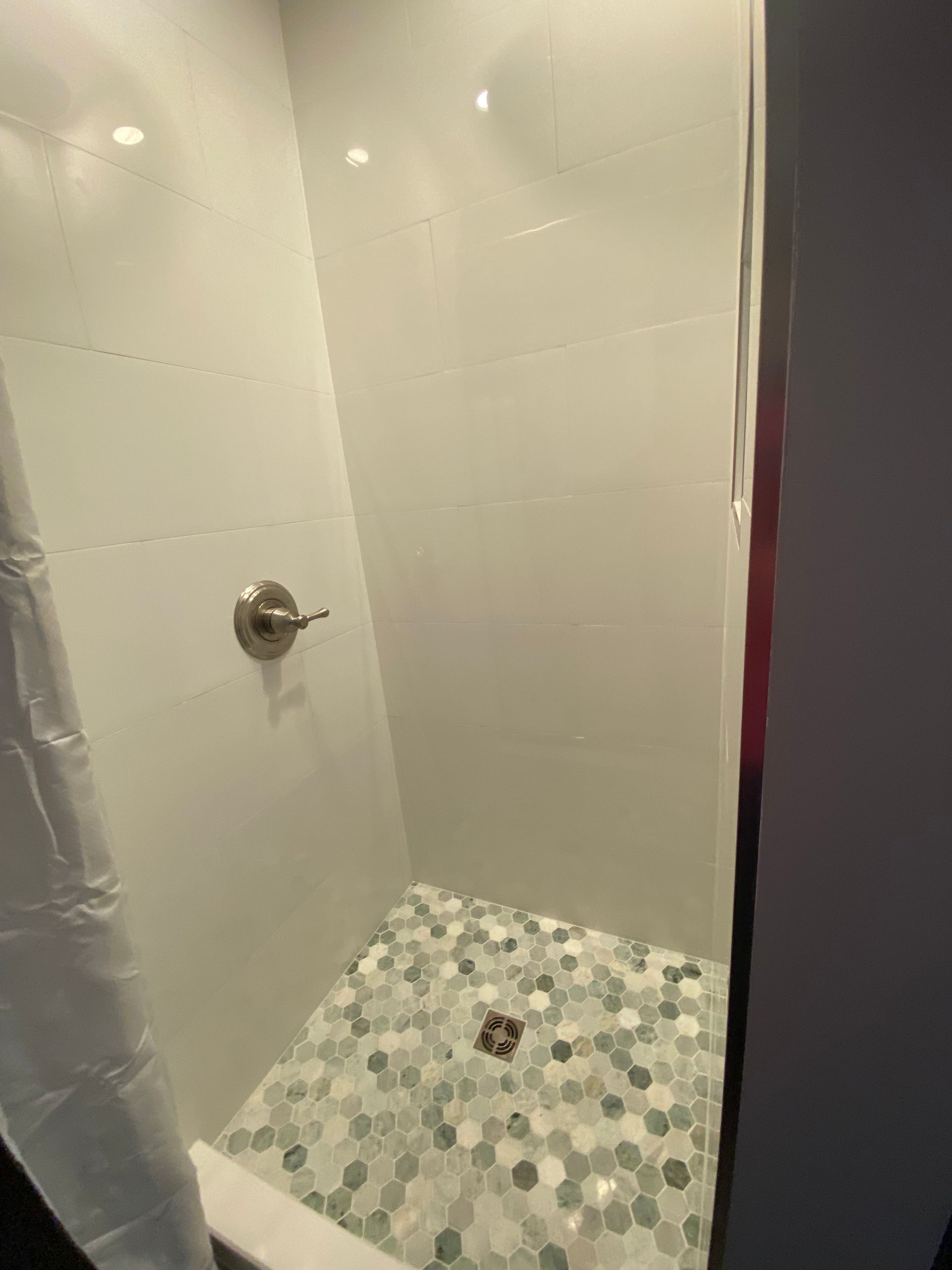 Shower with white walls, patterned floor tiles, and silver fixtures.