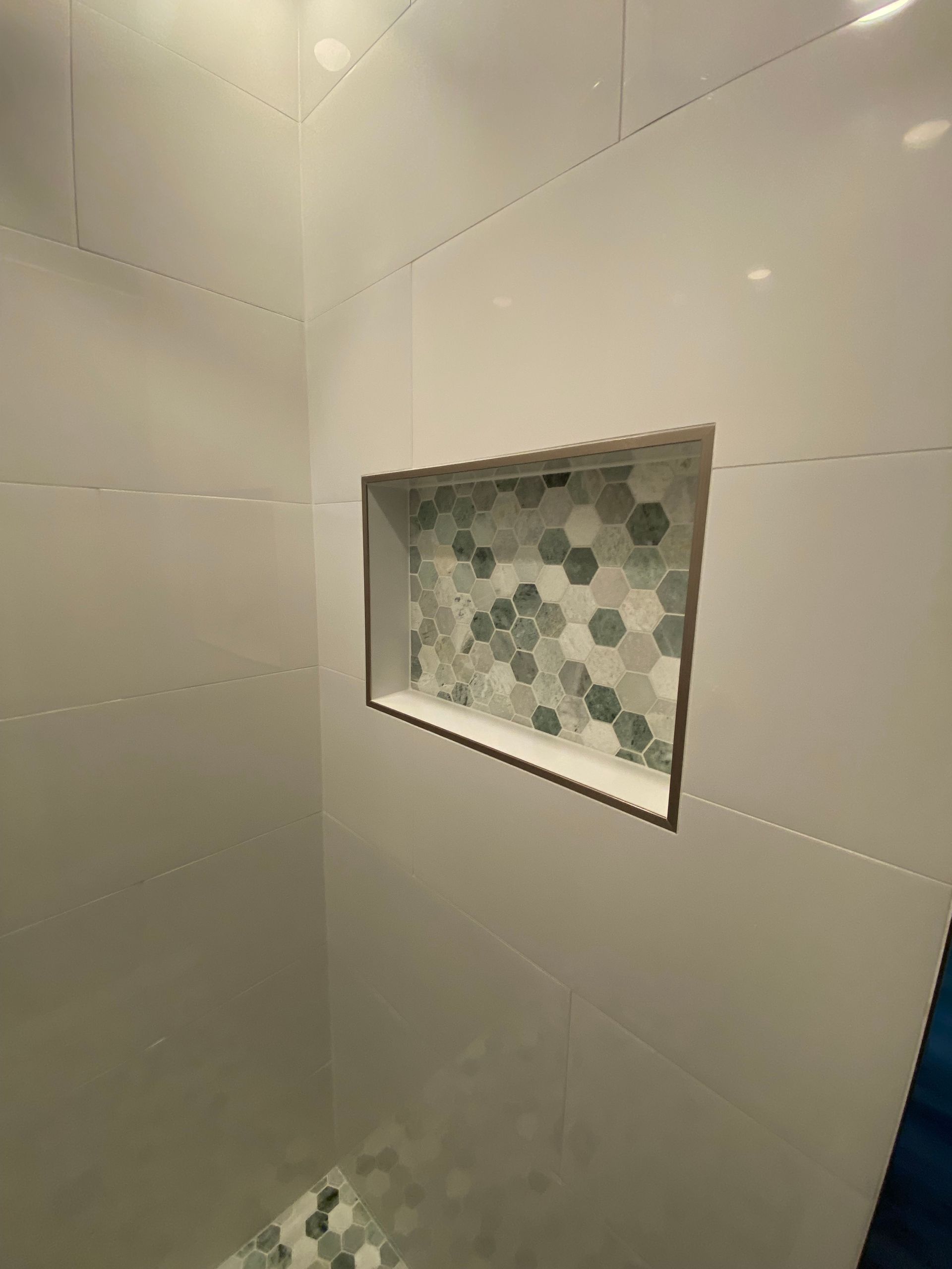 White tiled shower with a built-in hexagonal tile niche; grey and white mosaic tiles in the niche.