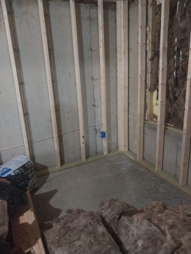 Framed interior wall construction with electrical box, insulation, and concrete floor.