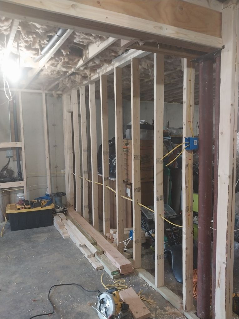 Interior view of a room under construction, framing a doorway. Studs, insulation, and electrical wiring are visible.