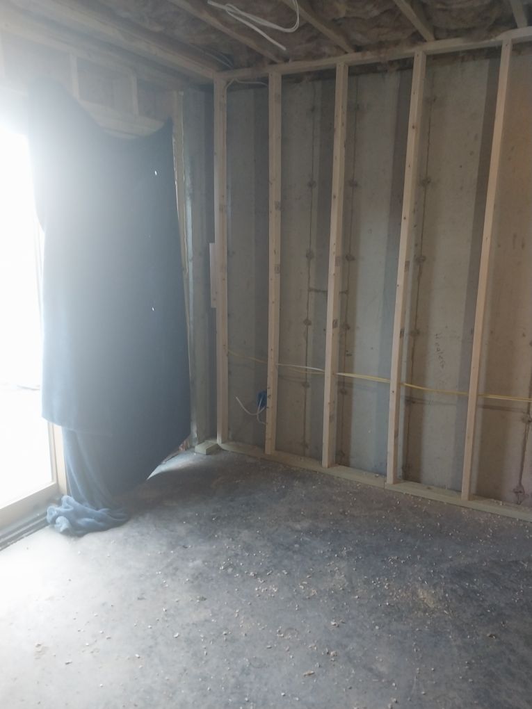 Unfinished room with exposed wooden studs, concrete floor, and sliding glass door; black material covers the door.