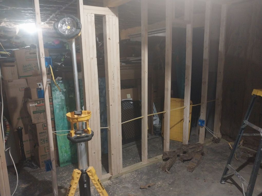 Basement renovation in progress: wooden studs frame a wall, with a work light and ladder present.