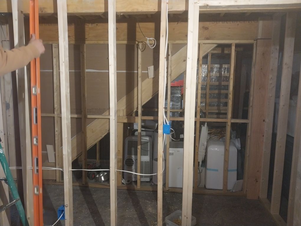 Framing of a wall in a basement, with a level being used. Shows exposed studs, stairs, and utilities.