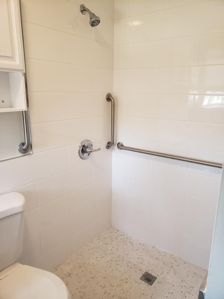 White accessible shower with grab bars and tiled walls. Toilet on left.
