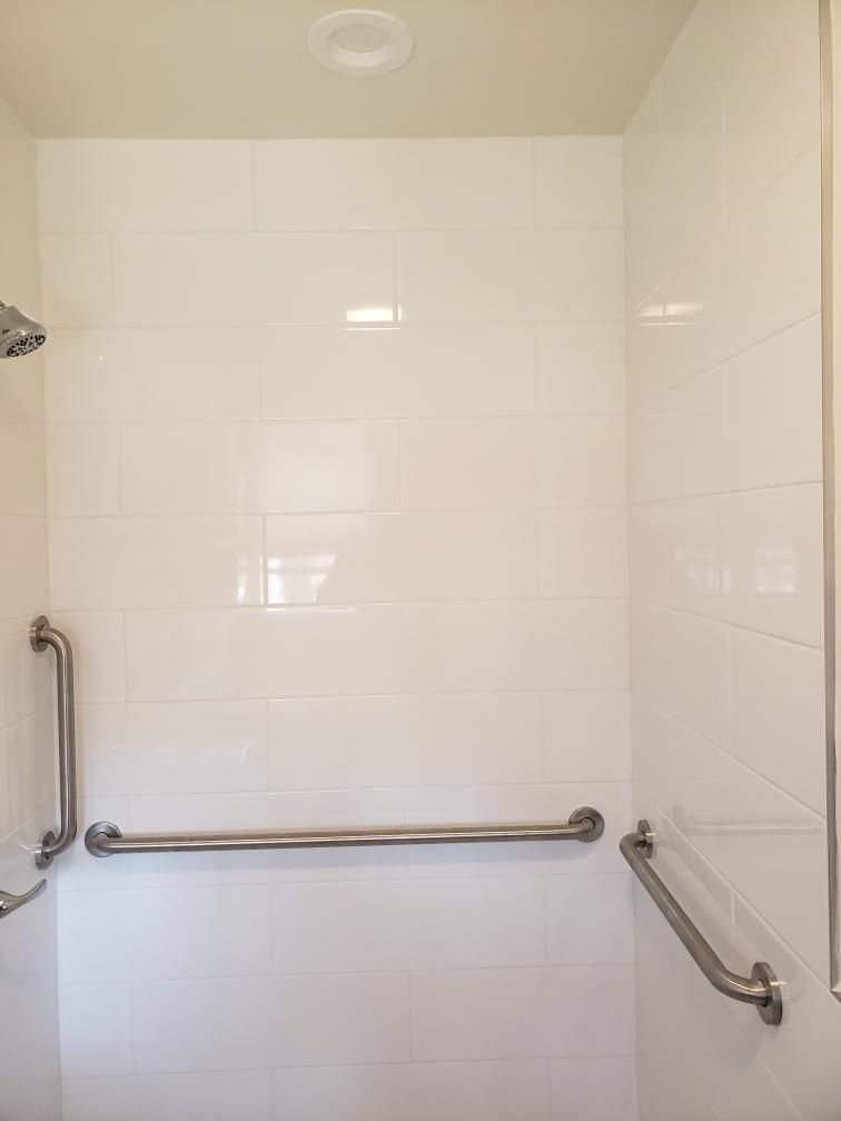 White tiled shower with silver grab bars for accessibility.