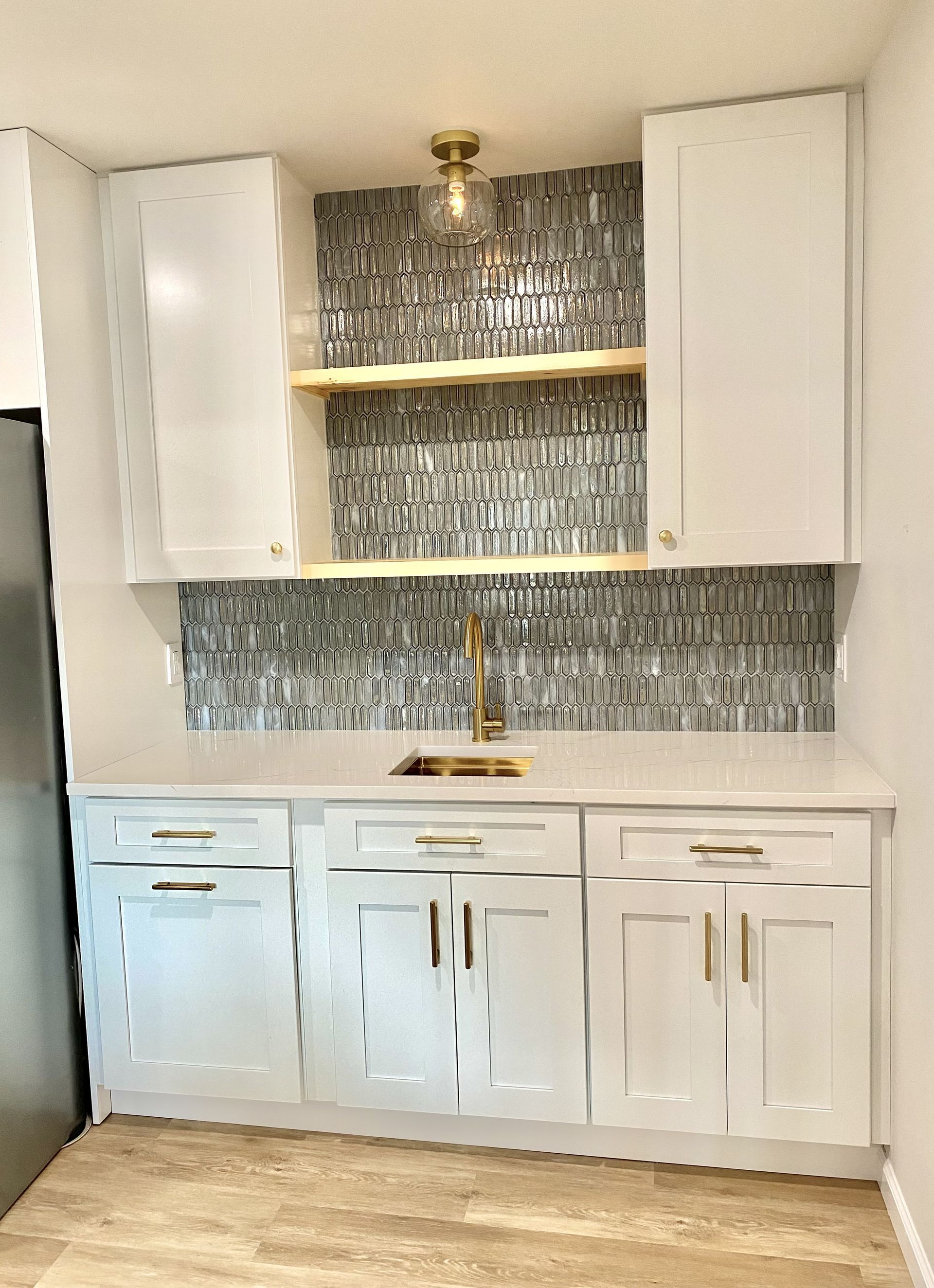 White kitchen cabinets with gold hardware, gold faucet, and gray mosaic backsplash.