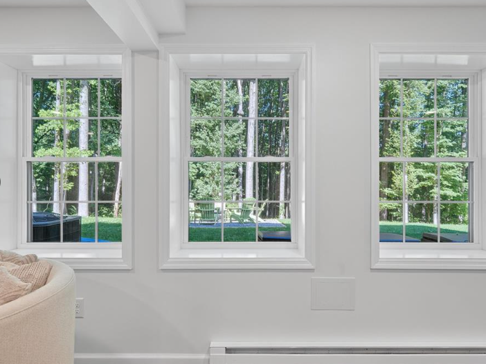 Three white-framed windows with a view of a green forest from inside a white room.