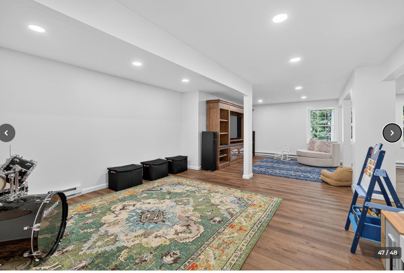 A finished basement with a drum set, area rug, built-in entertainment center, seating, and hardwood floors.