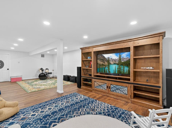 Basement with built-in entertainment center, TV, speakers, drum set, and blue patterned rug.
