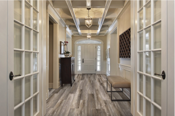 Hallway with wood-look floor, white doors, and a detailed ceiling, leading to a front door.