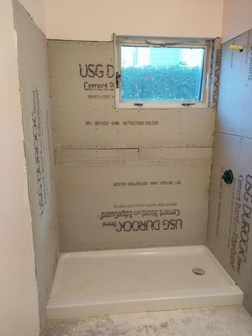Shower stall under construction, featuring cement backerboard, window, and shower base.