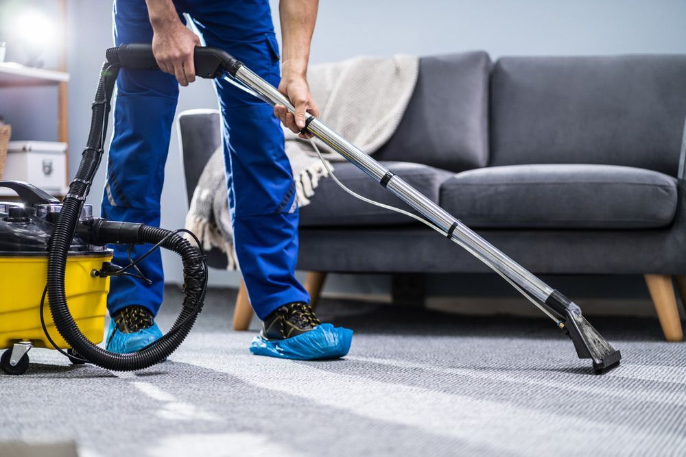 A Man Is Using A Vacuum Cleaner To Clean The Carpet In A Living Room — Cleaner Near Me in Woombye, QLD