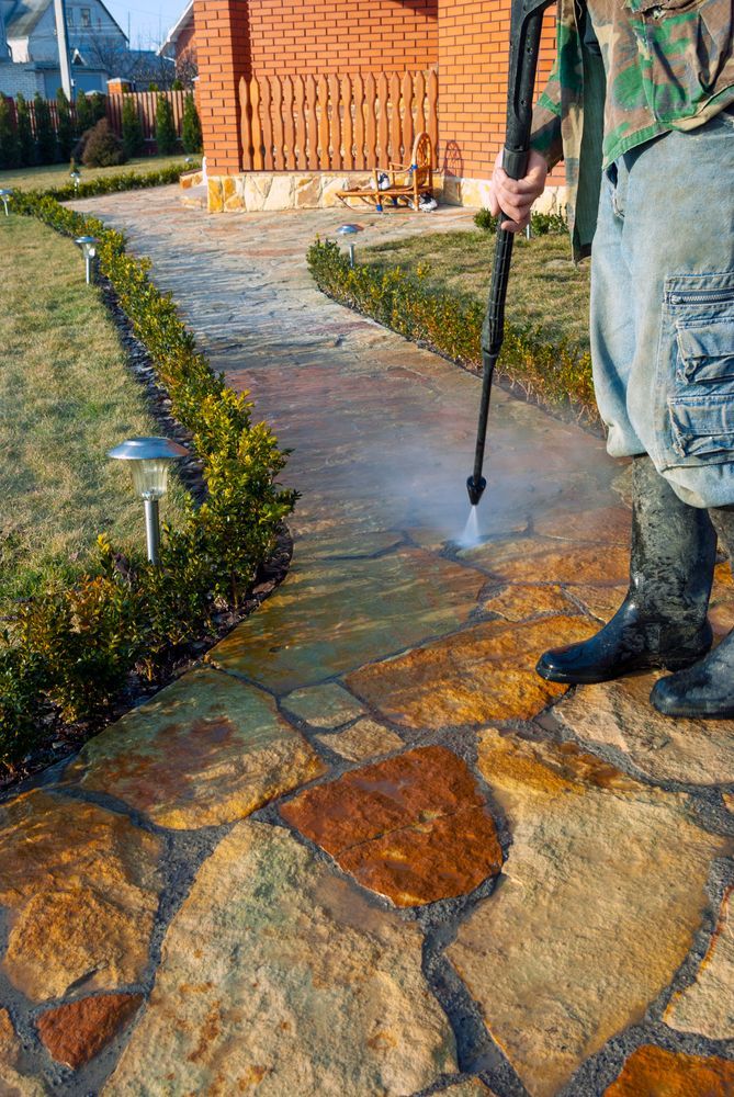 A Man Is Cleaning A Stone Walkway With A High Pressure Washer — Cleaner Near Me in Woombye, QLD