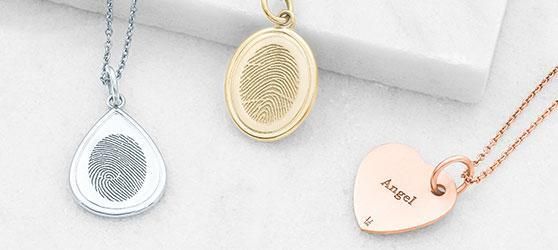 Three necklaces with fingerprint pendants are sitting on a table.