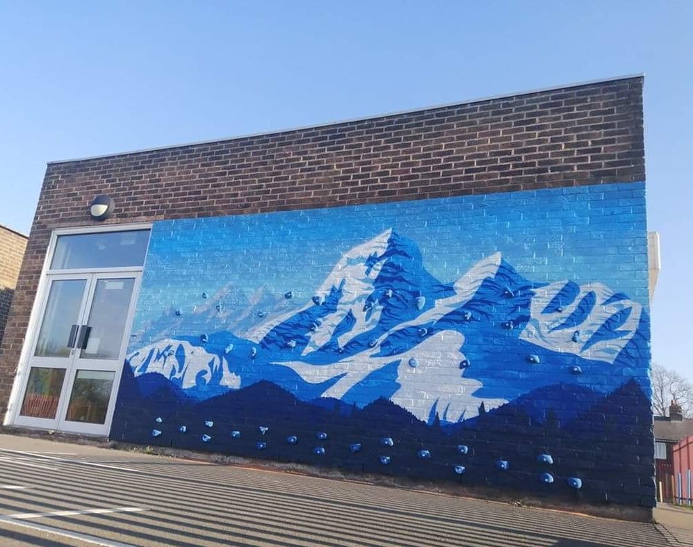Mural of snowy mountains in shades of blue on a brick building wall, next to a doorway.