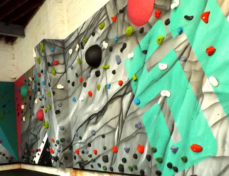 Climbing wall with colorful holds. Gray and teal panels with black lines; red, blue, green, and black holds.
