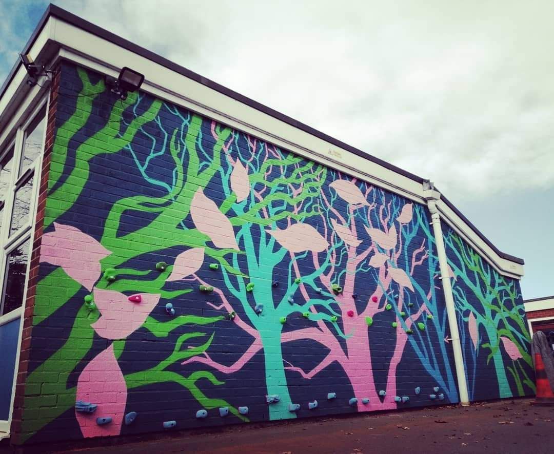 Mural on a building exterior depicts colorful trees against a dark blue background; green and pink leaves and branches.