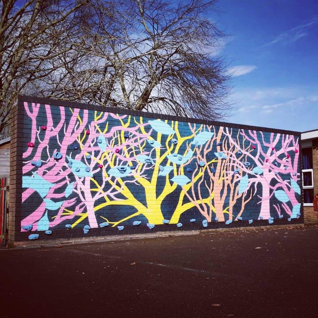 Colorful mural on a brick wall depicting stylized trees in pink, yellow, and blue against a blue sky.