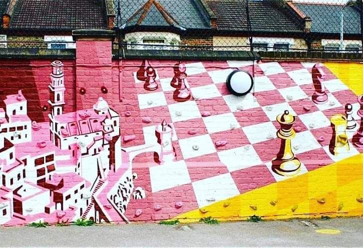 Street art mural depicting a pink chessboard with chess pieces and a city landscape.