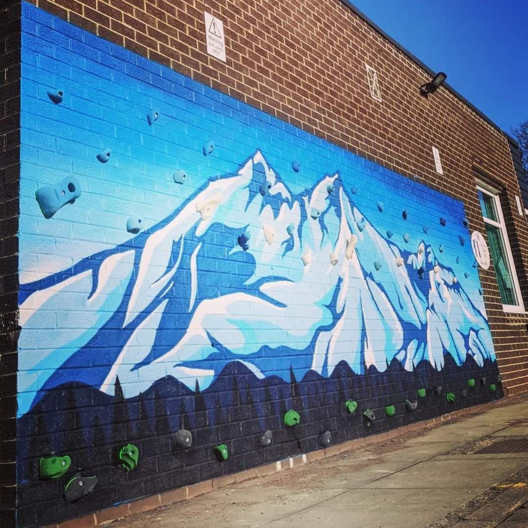 Climbing wall mural of snowy mountains on a brick building with climbing holds.