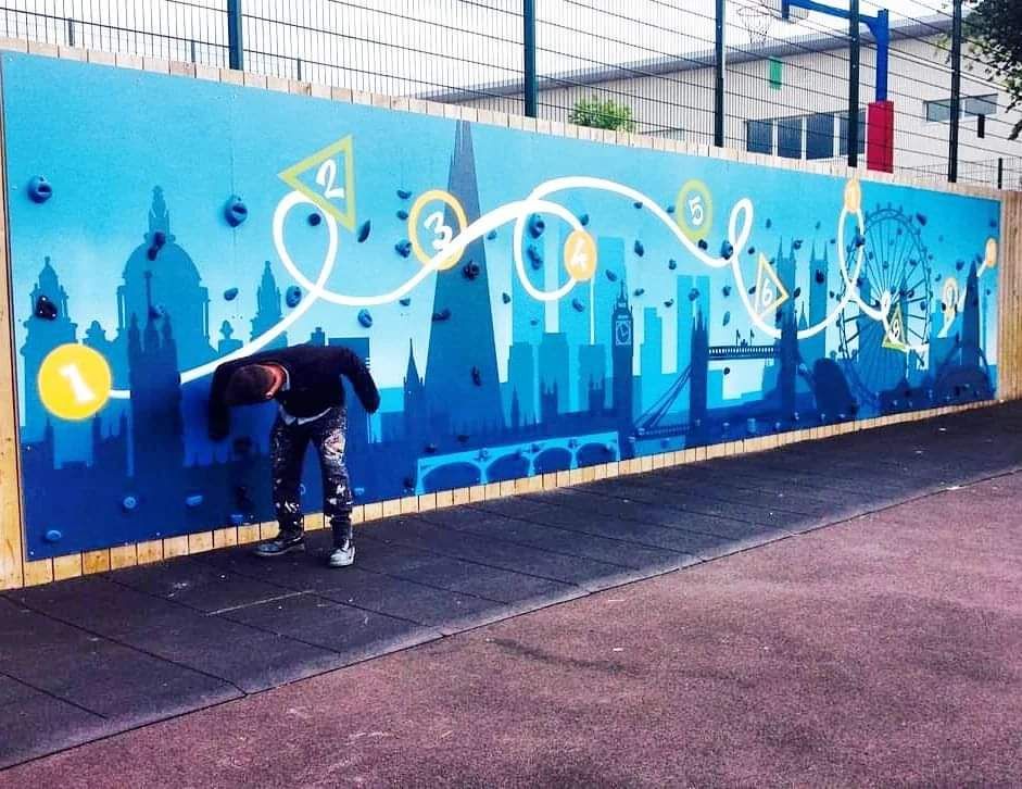 A child climbs a blue climbing wall with a London skyline design.