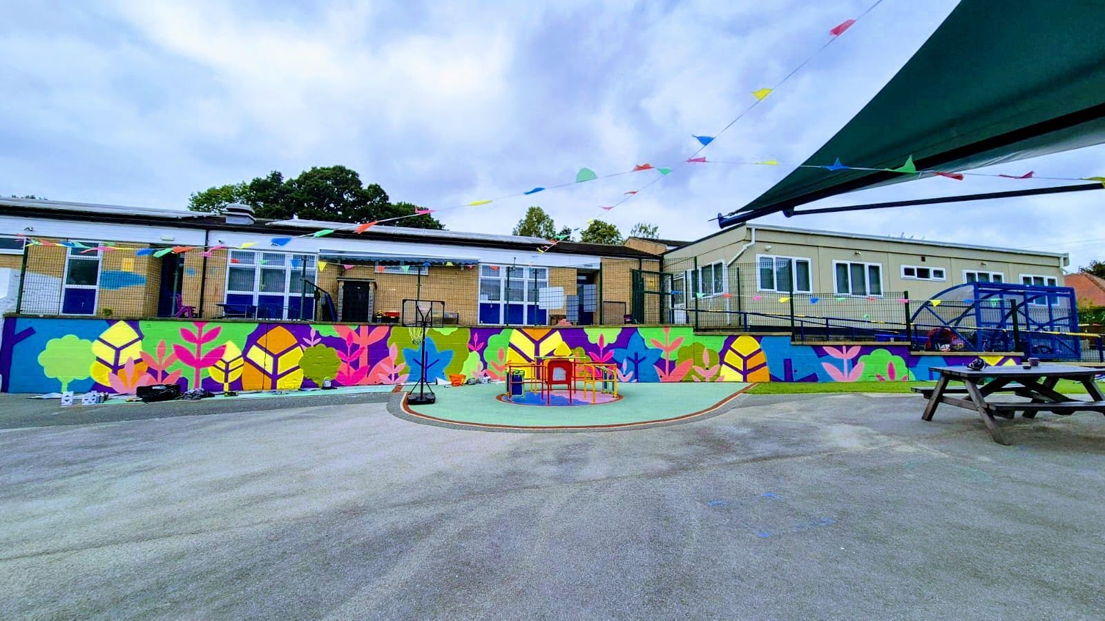 Exterior view of a school building with a colorful mural, playground, and canopy.