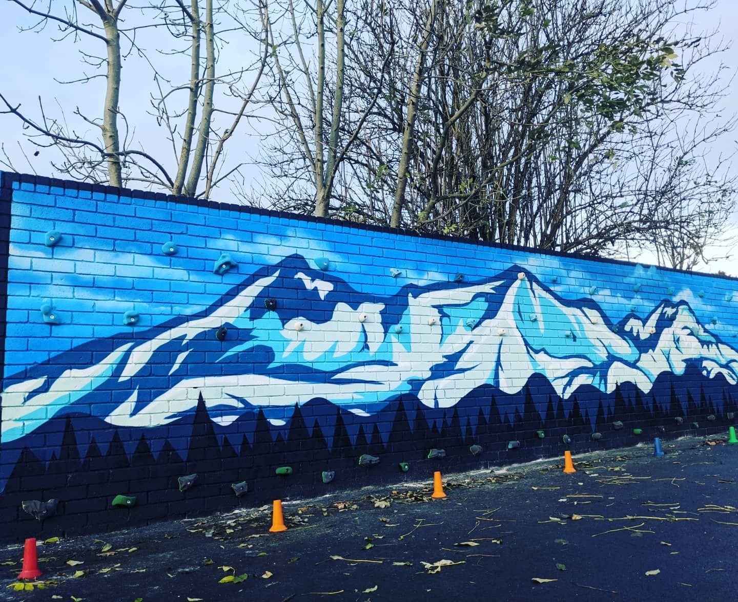 Mural of snow-capped mountains painted on a brick wall, with dark trees in the foreground.
